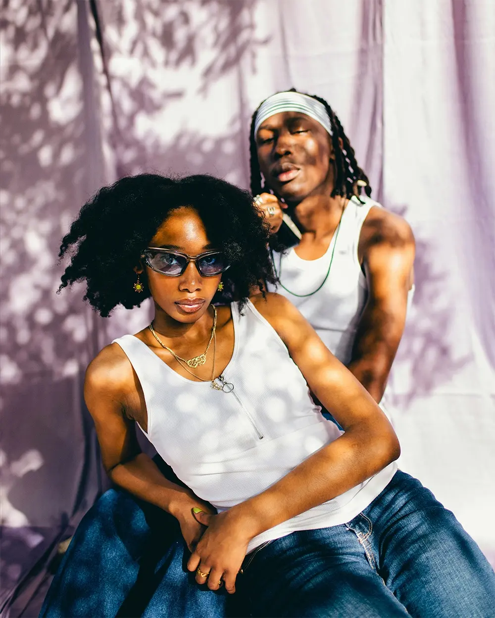 Two models in white tank tops against a purple backdrop