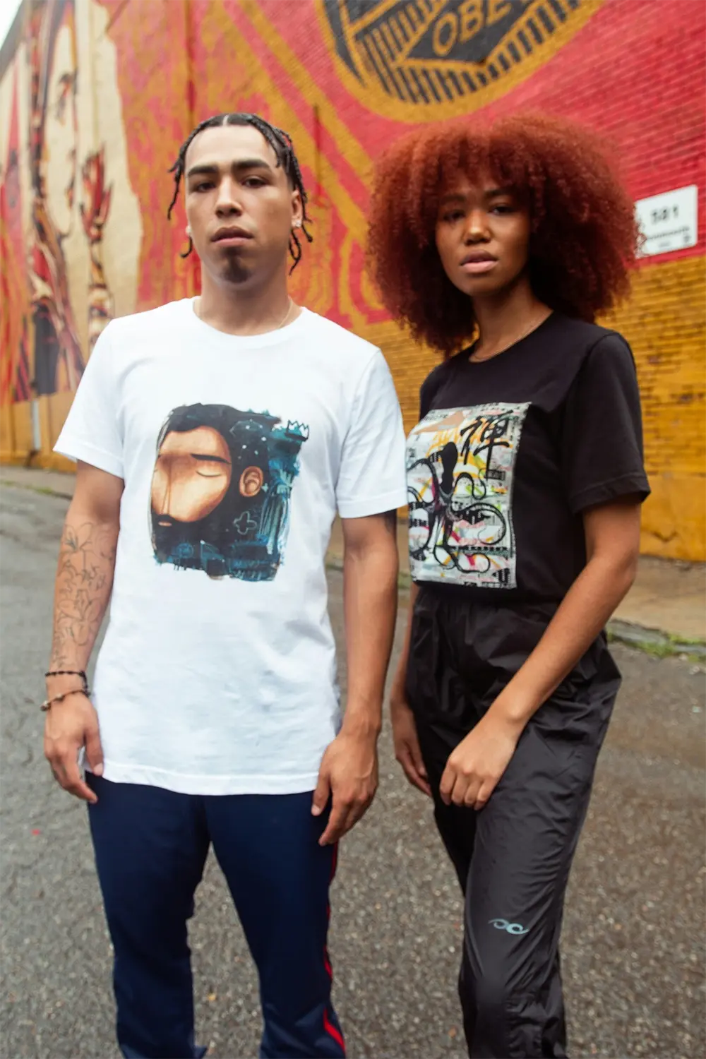 Man in white graphic t-shirt and woman with curly hair in black outfit against colorful mural